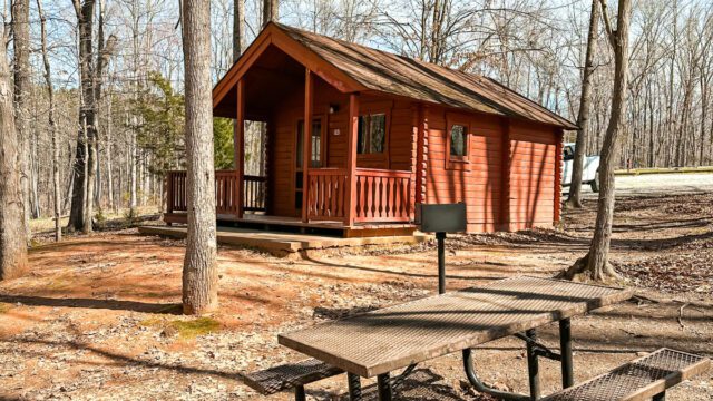 A red cabin with a peaked roof with a brown picnic bench in front