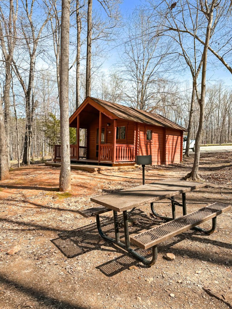 A red cabin with a peaked roof with a brown picnic bench in front