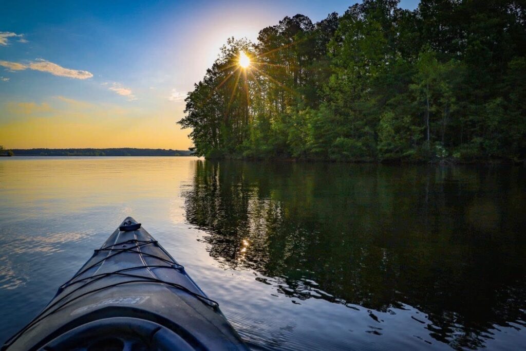 The tip of a kayak on a lake surrounded by green trees