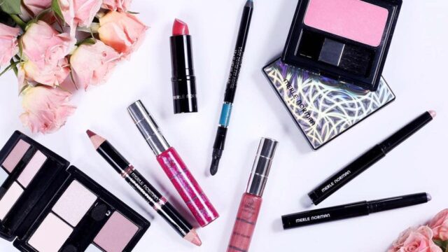 A selection of eye shadow palettes, lipsticks, and eyeliner pencils displayed on a white background with two bouquets of pink roses.