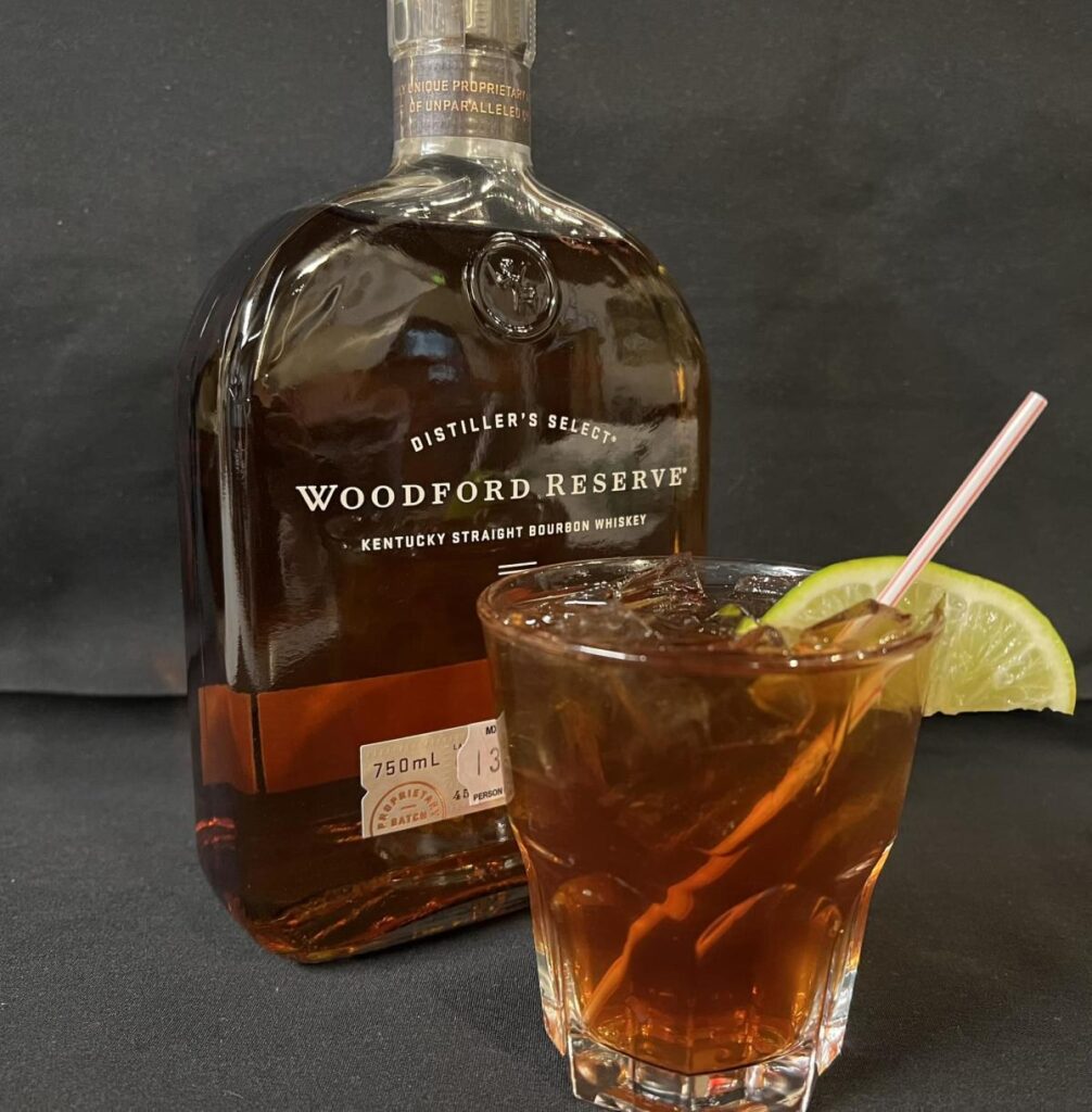 A full bottle of Woodford Reserve whiskey and a glass of whiskey with a lemon wedge placed in front