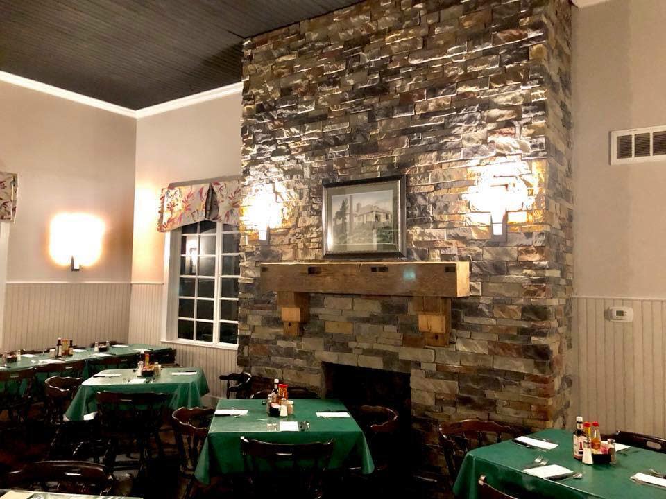 A large stone fireplace in a restaurant surrounded by tables with green tablecloths