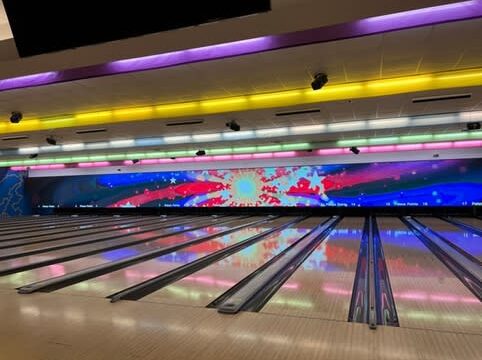 Empty lanes at a bowling alley with yellow and purple overhead lights