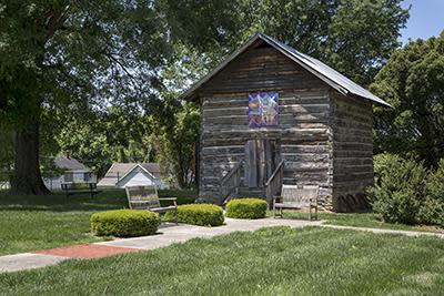 A small wooden building with a quilt painting above the doorway