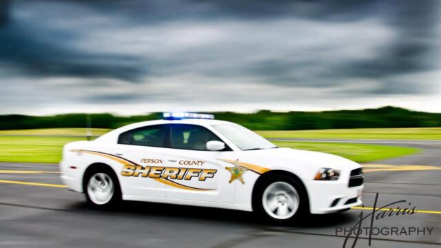 A white Person County sheriff car driving on a paved road with dark clouds in the background
