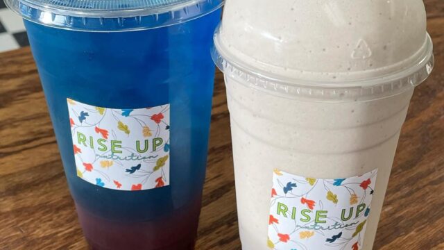 A blue iced beverage in a plastic to-go cup and a thick blended beverage in a plastic to-go cup