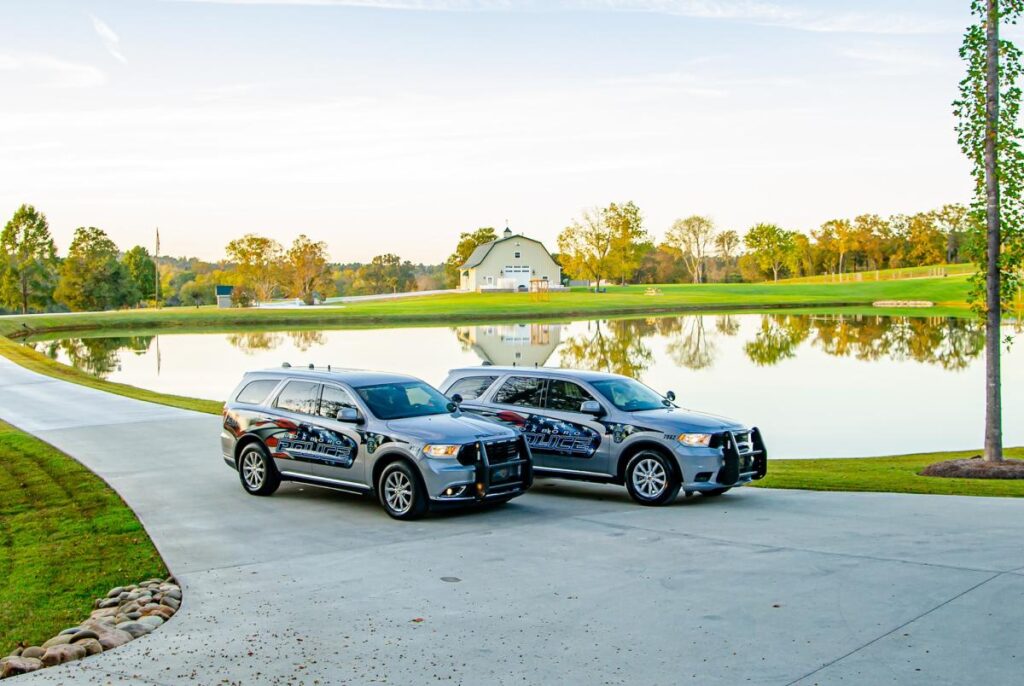 Two silver police cars parked on a concrete driveway by a lake