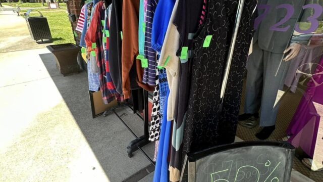 Two hanging racks with clothing displayed outside a store on the sidewalk