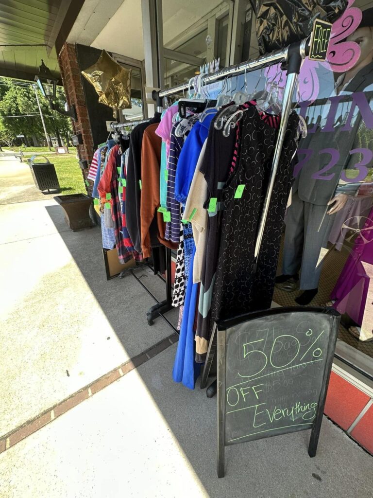 Two hanging racks with clothing displayed outside a store on the sidewalk