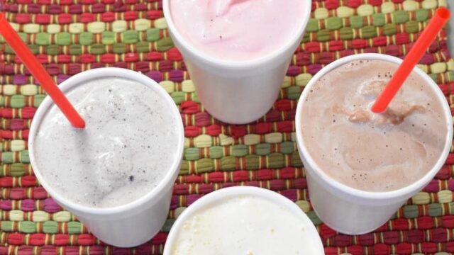 Four different flavors of milkshakes in Styrofoam cups sit on a colorful placement