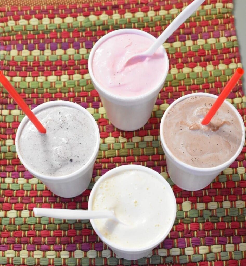 Four different flavors of milkshakes in Styrofoam cups sit on a colorful placement