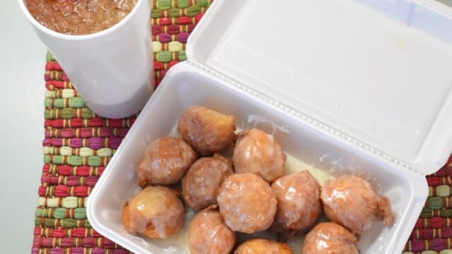 A white Styrofoam container with a dozen glazed donut holes and a Styrofoam beverage site on a colorful placemat