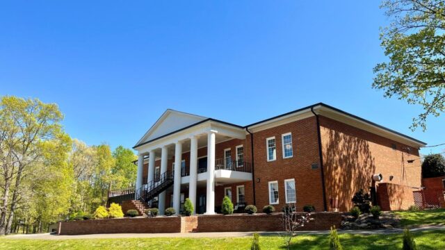 A large two-story red brick building with a white portico and large split staircase in front