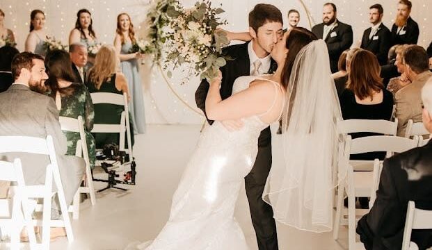 Surrounded by guests, a bride and groom kiss after the wedding ceremony