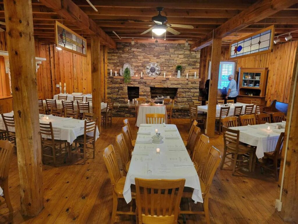 A restaurant with wooden walls and floors filled with wooden tables and white tablecloths