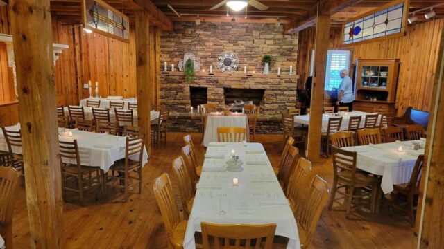 A restaurant with wooden walls and floors filled with wooden tables and white tablecloths