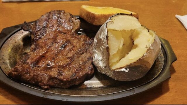 An oval-shaped metal plate with steak, a baked potato and slice of toast