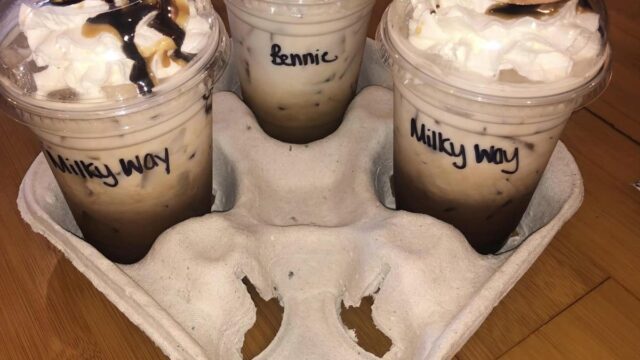 Three coffee drinks topped with whipped cream in a cardboard to-go container