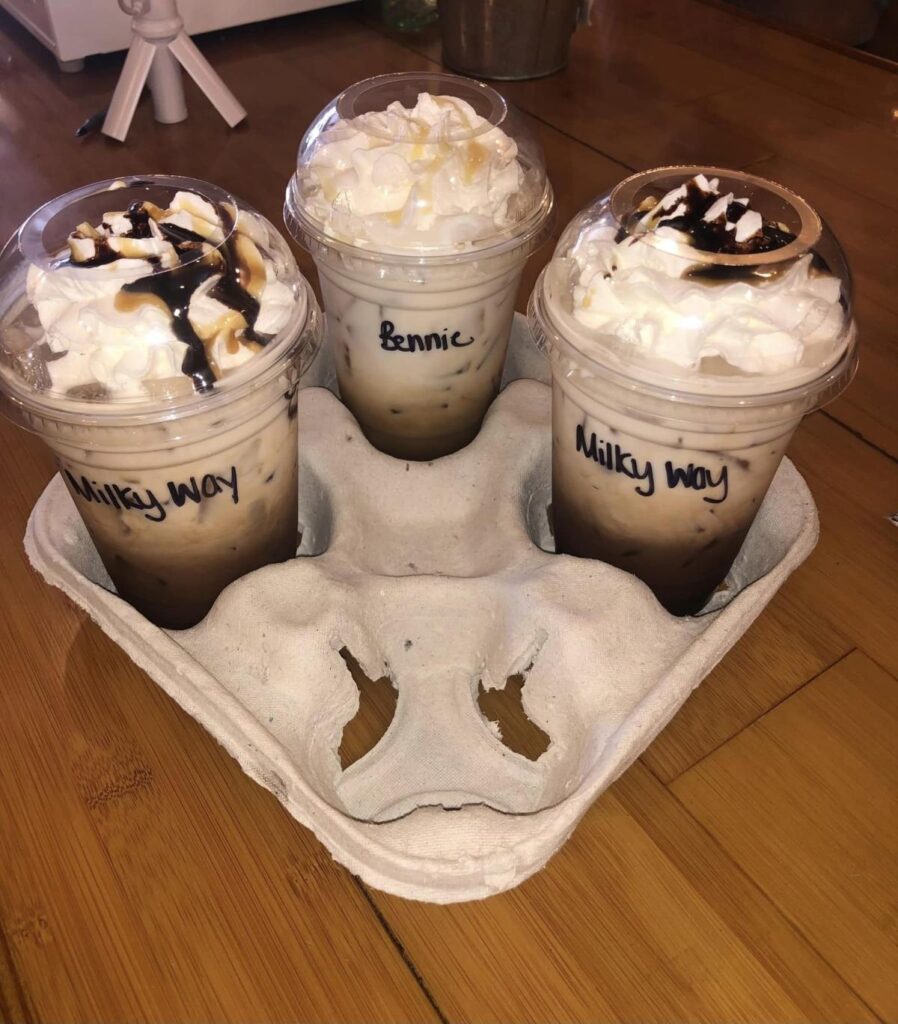 Three coffee drinks topped with whipped cream in a cardboard to-go container