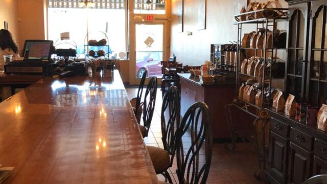 A coffee shop with a long wooden counter with chairs pulled up