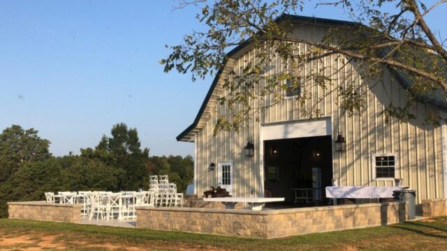 A cream-colored barn with an attached outdoor patio covered with white tables and chairs