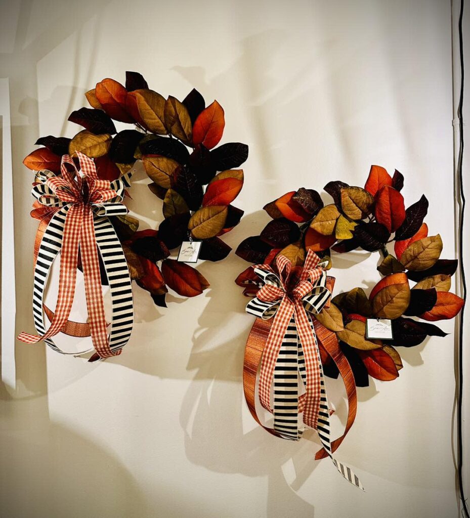 Two wreaths made of fall leaves and tied with orange, black, and white bows