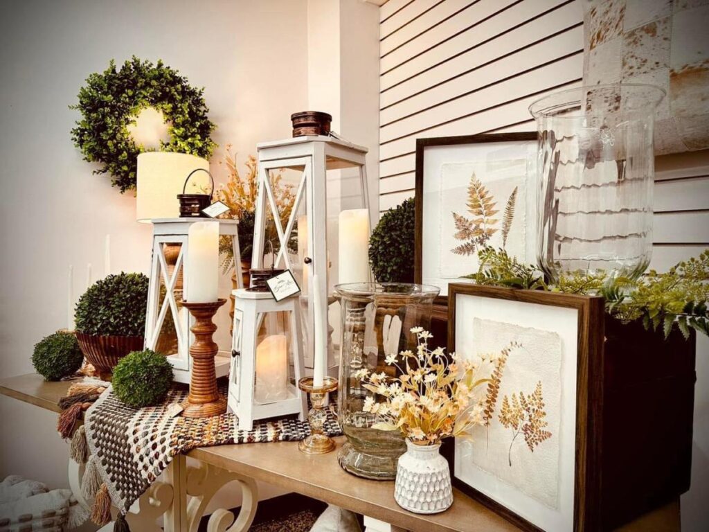 A table display of home decor items including candles, prints and greenery