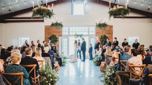 A bride and groom get married in front of seated guests in a building with rustic decorations