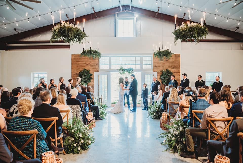 A bride and groom get married in front of seated guests in a building with rustic decorations