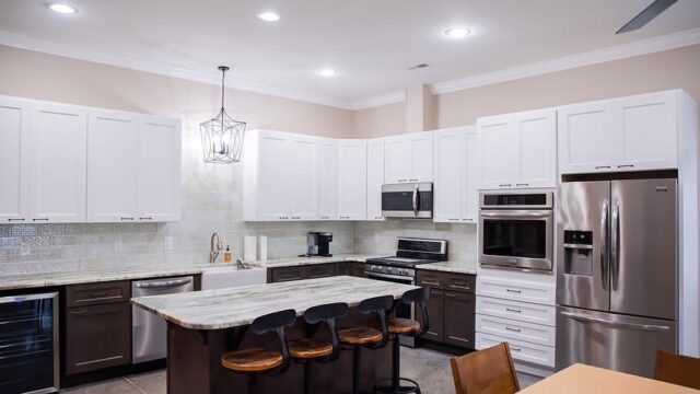 A kitchen with white upper cabinets, a gray stone countertop and dark lower cabinets