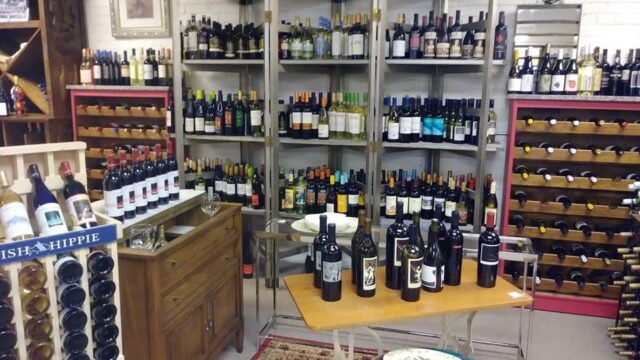 A wine shop with displays of wine along the wall and a small table with bottles of wine for sampling