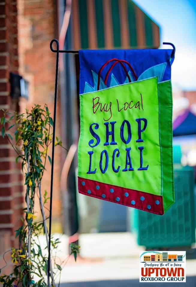 A brightly colored vinyl sign reading 'Buy local, shop local' hangs outside.