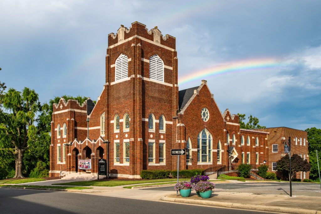 A red brick church with a rainbow in the sky