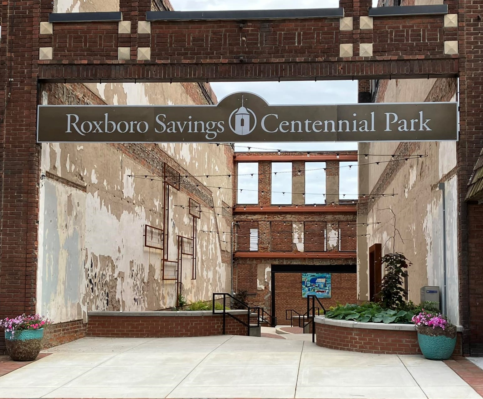 A sign for Roxboro Savings Centennial Park spanning two brick buildings